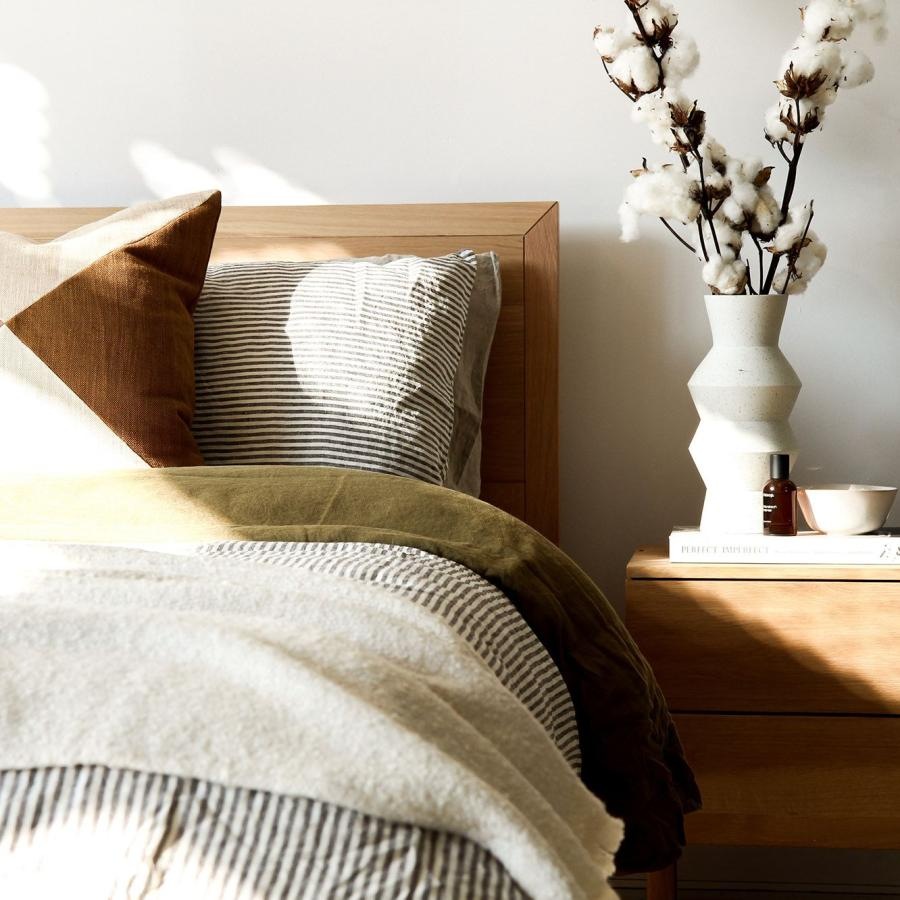 swath of sunlight shines across a well made bed and bedside table with a vase of cotton plants